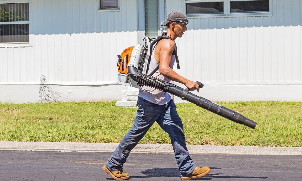 man walking along the road using a leaf blower