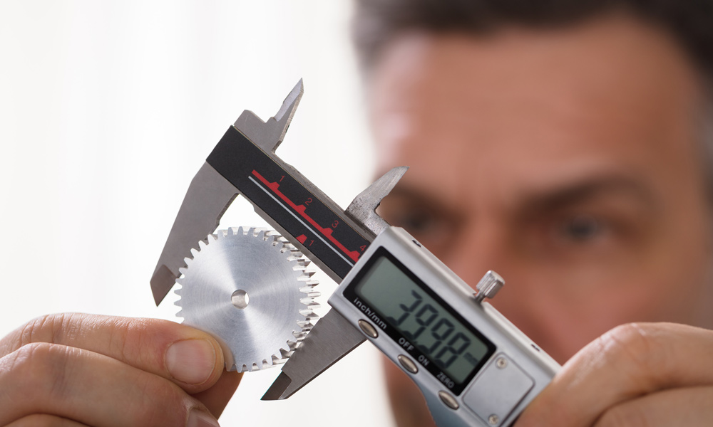 a man measuring a metal cog with a digital Caliper