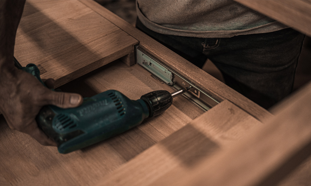 A drill screwing a screw into a piece of furniture