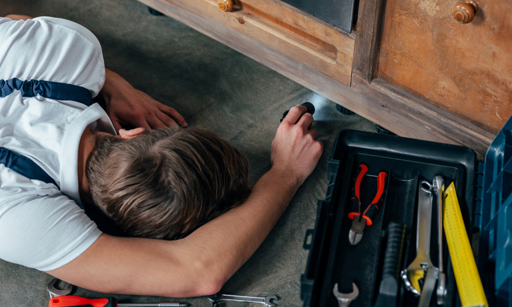 workman using a Flashlight to look under a unit