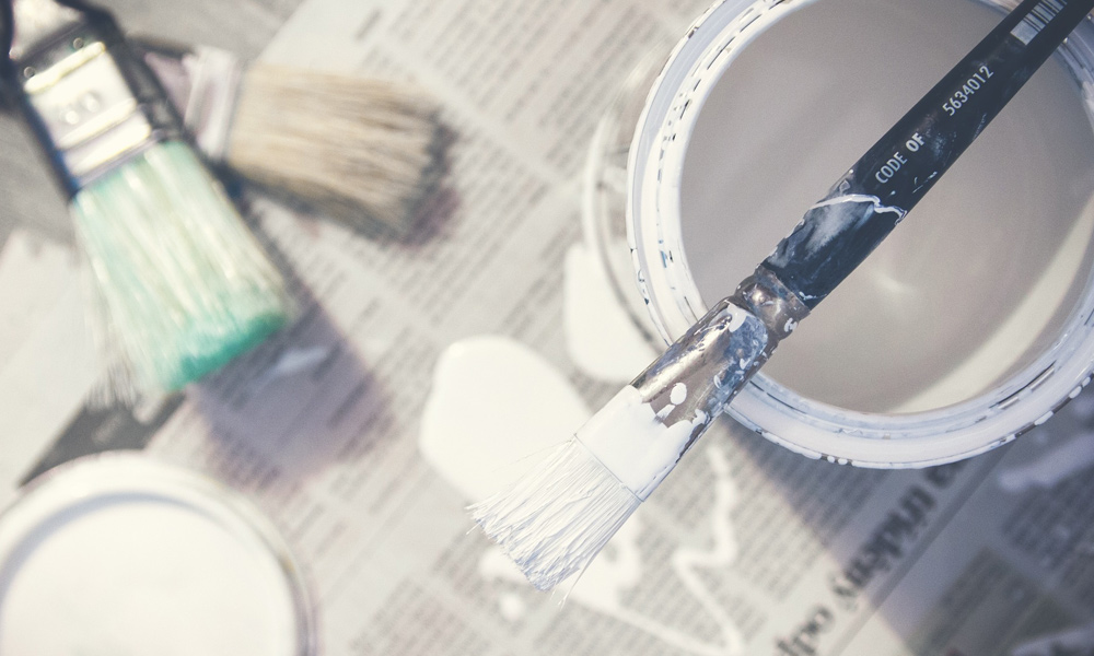 paint brush on top of a white paint pot