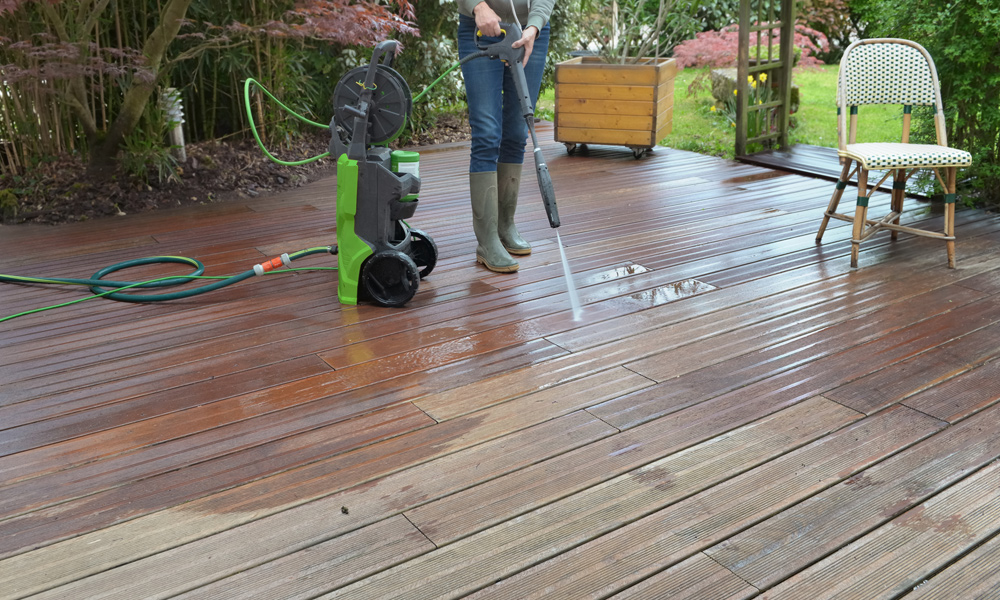 A woman jet washing her decking with a pressure washer