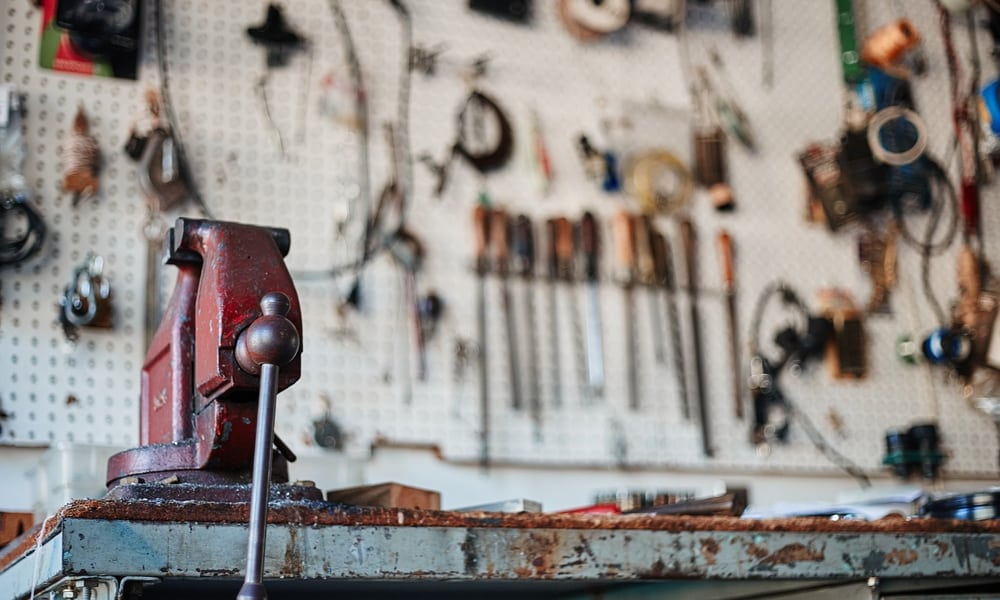 A bench vise mounted to a work table with tools in the background